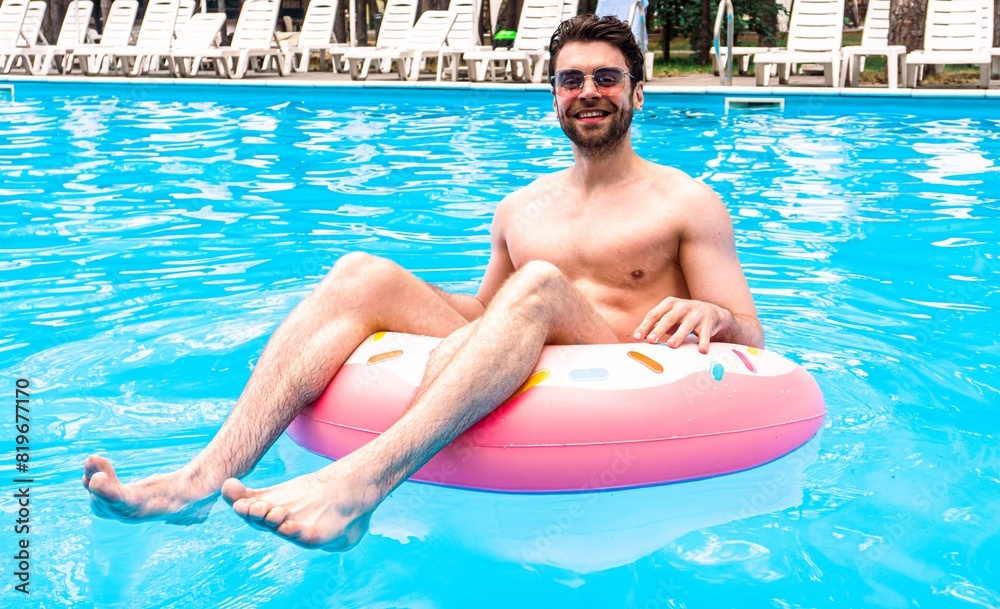 Smiling bearded guy enjoying the rest in the swimming pool while using inflatable ring. Man in sunglasses. Summertime, holidays, lifestyle concept
