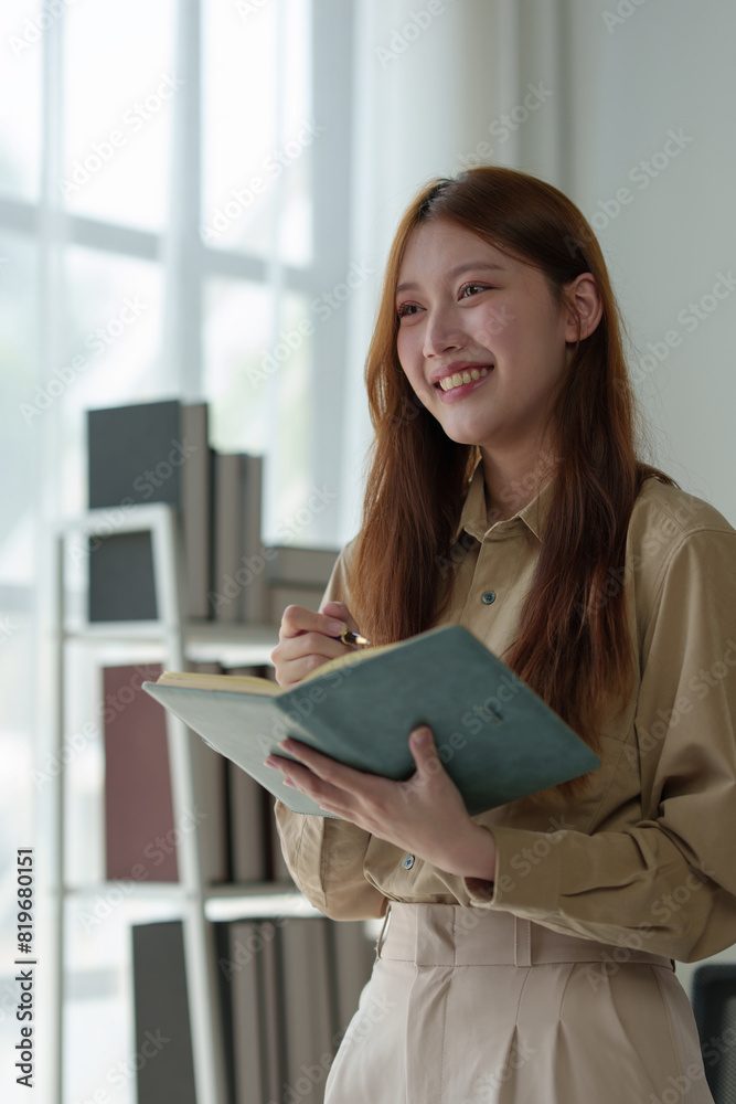 Confident businesswoman standing holding notebook. Concepts, ideas working with laptop in office. Happy beautiful Asian business woman Charming smiling female office worker. Confident businesswoman standing holding notebook. Concepts, ideas working with laptop in office. Happy beautiful Asian business woman Charming smiling female office worker.