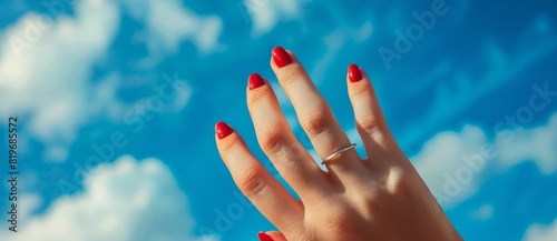 Photo of A woman's hand with red manicure on blue sky
