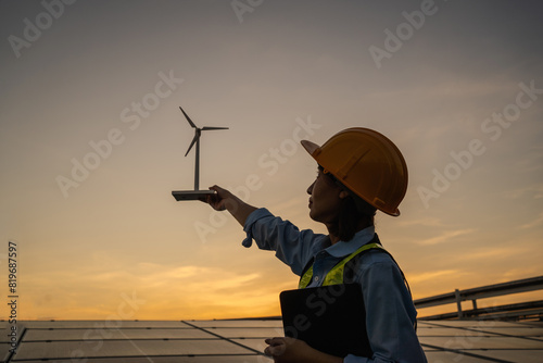 A woman wearing a hard hat is holding a wind turbine in her hand. Concept of innovation and progress, as the woman is likely involved in the development or maintenance of renewable energy sources photo