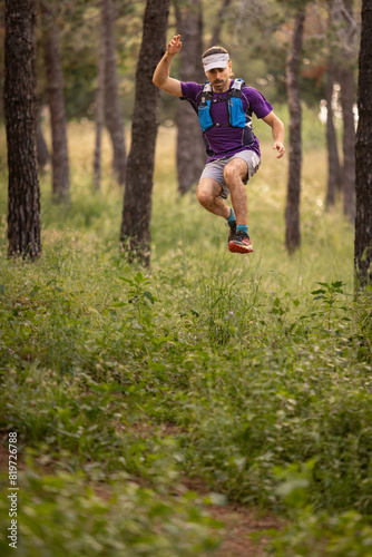 A man is jumping over a grassy field. He is wearing a purple shirt and blue shorts
