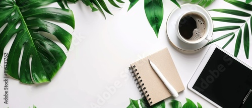 Topdown view of notepad, coffee, tablet, and green leaves on a white background
