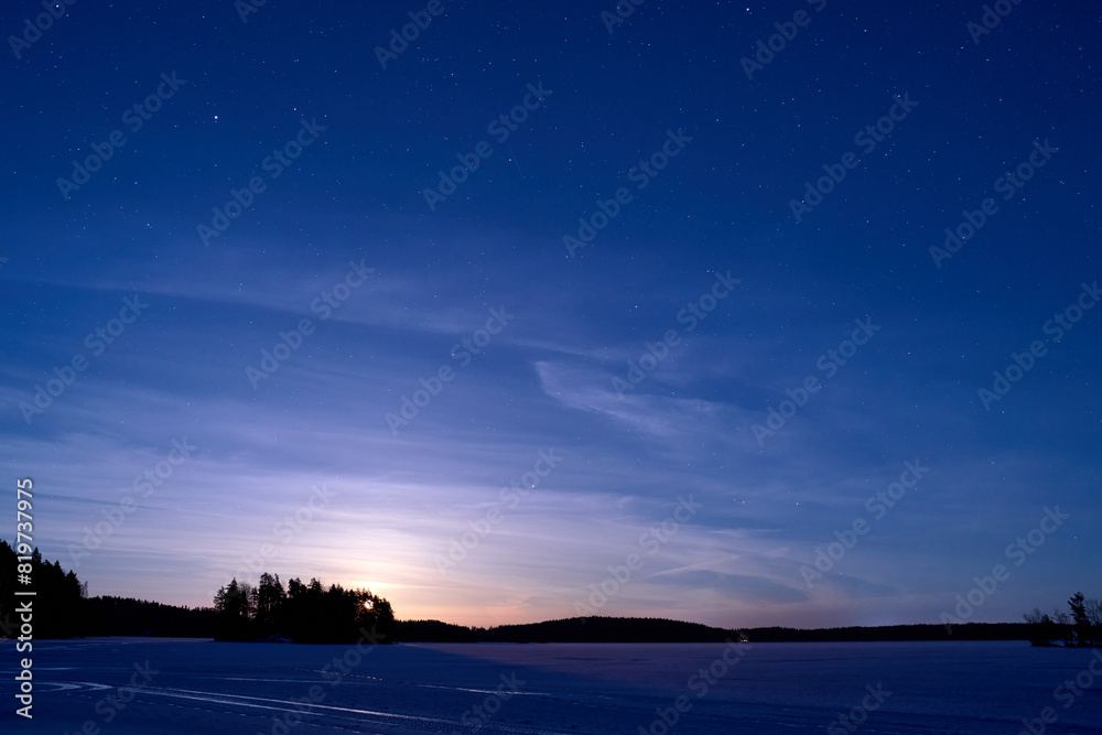 Fototapeta premium Serene nighttime winter landscape with a frozen lake and blue sky