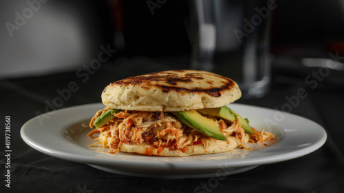 Savory venezuelan arepa stuffed with juicy shredded chicken and fresh avocado slices on a white plate with a black background