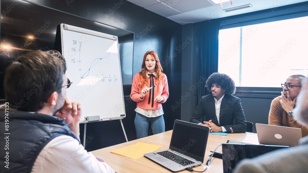 Businesswoman explaining line graph on whiteboard to diverse colleagues in office Businesswoman explaining line graph on whiteboard to diverse colleagues in office