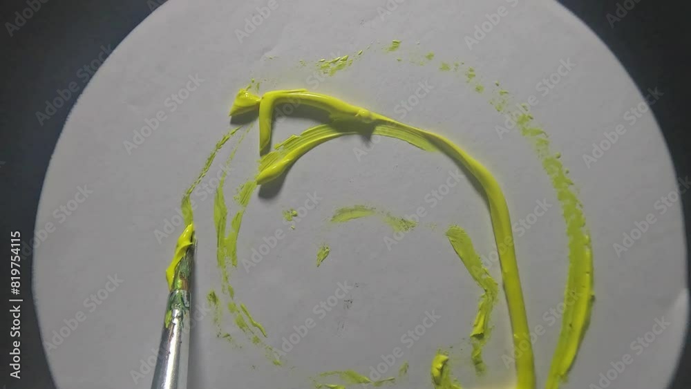 Top view of artist brush spreading the yellow color on a rotating white table with blur background