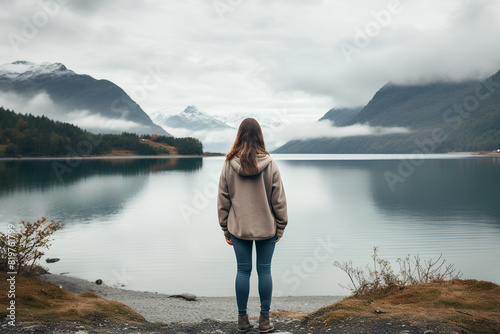 young woman standing overlooking the lake, with mountain landscape and cloudy weather  photo