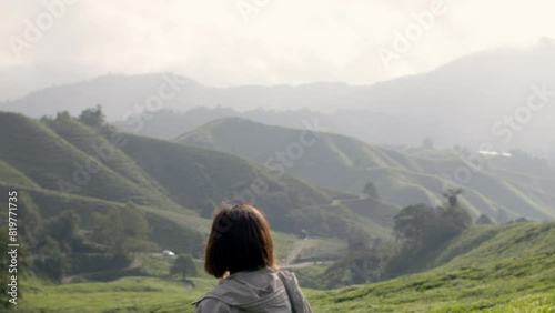 Asian woman walking in the green tee plantation field with mountains in the background photo