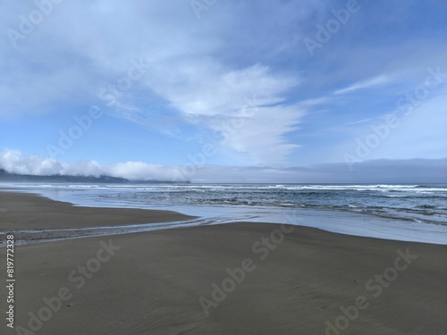 Sandy beach and the calm waters of the sea with the horizon and a cloudy sky in the background