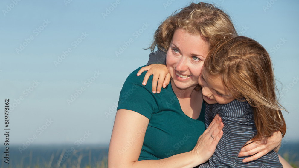 young mother with her little daughter piydoors looking to the left smiling and hugging young mother with her little daughter piydoors looking to the left smiling and hugging