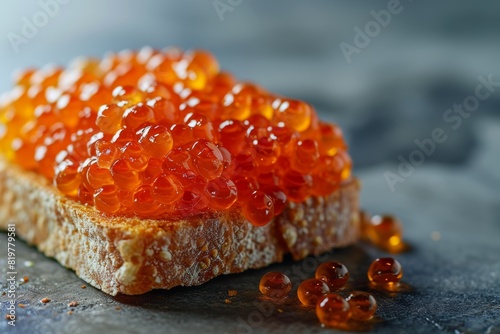 Close-up view of red caviar on a slice of multigrain toast, with additional caviar pearls scattered on a dark surface