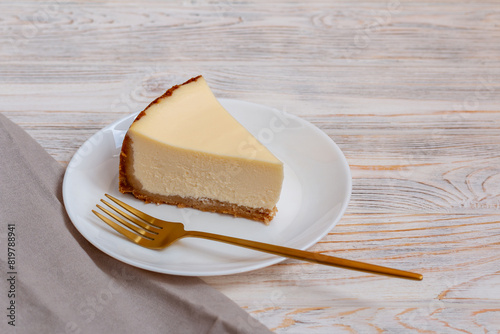 A piece of cheesecake New York with a golden fork on a wooden table.