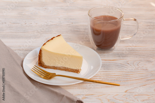 A piece of cheesecake New York and cup of cocoa with a golden fork on a wooden table.