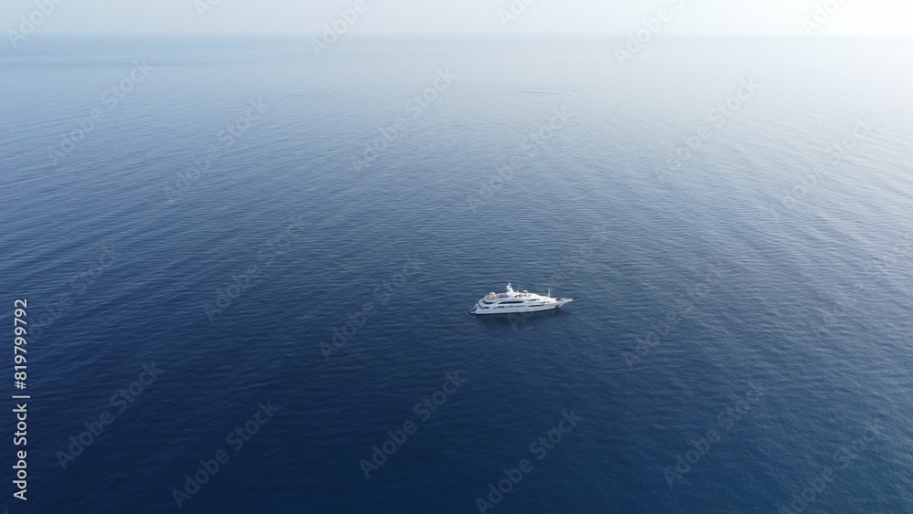 Aerial shot of a white boat sailing in the open expanse of blue ocean. Aerial shot of a white boat sailing in the open expanse of blue ocean.