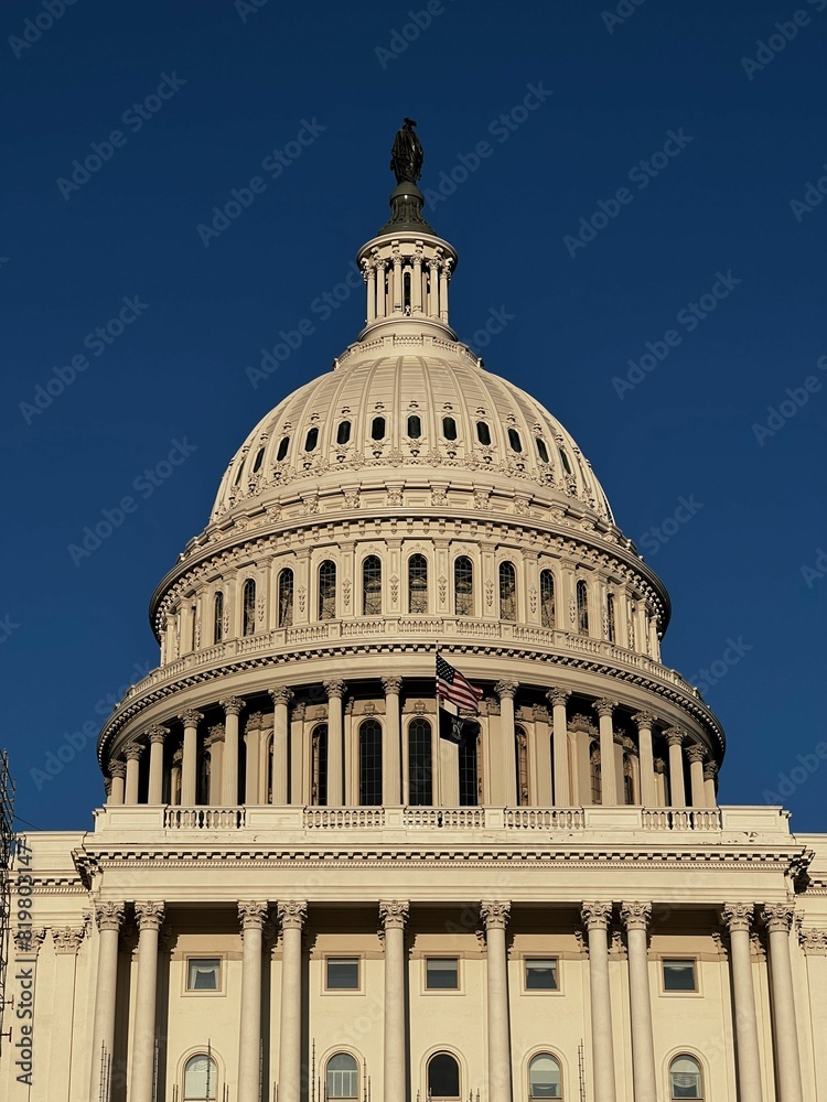 Obraz premium Blue sky over the US Capitol Building with waving national flag - Washington DC, United States