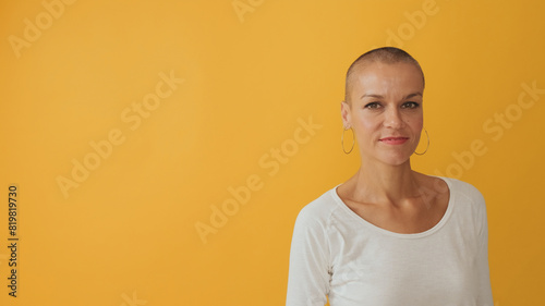 Young hairless woman looking at camera with smile, advertising space, isolated on yellow background in studio