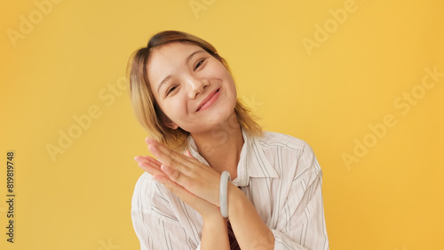 Surprised young woman dressed in shirt and tie covers her mouth with her hand and claps her hands isolated on yellow background in studio © Andrii Nekrasov