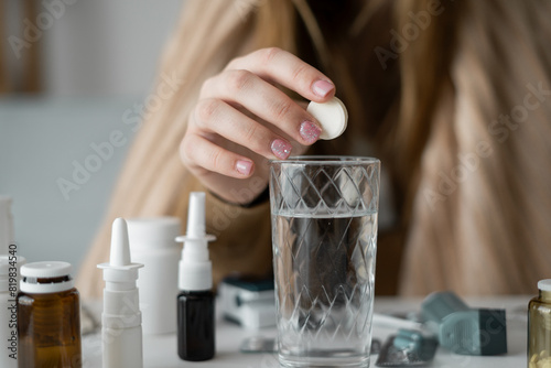 large Caucasian woman is wrapped in a blanket, trembling, feeling unwell, and has a high temperature. close-up of a hand throwing an effervescent soluble tablet into a glass.