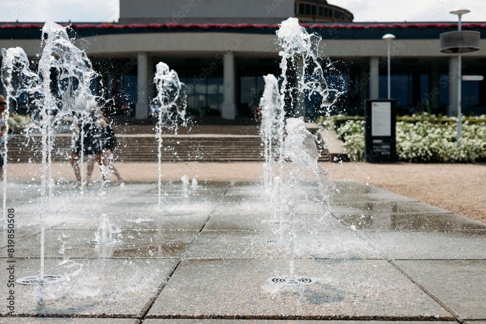 Water droplets spread from the fountain in the air. Splashing water from a fountain in the park. Vertical fountain jets in the sidewalk on the square in the city park.
