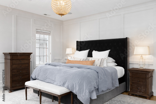 A bedroom detail with cozy decor, wainscoting walls, and a gold and crystal chandelier hanging above the bed. photo