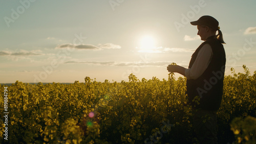 At sunset, a woman farmer is seen standing in a rapeseed field, enjoying the beautiful rural landscape.