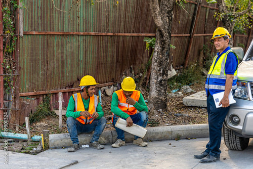 Team of civil engineers or workers in safety suits taking rest after a long day in a construction site waiting for the next assignment. Cooperation among construction workers in a factory.