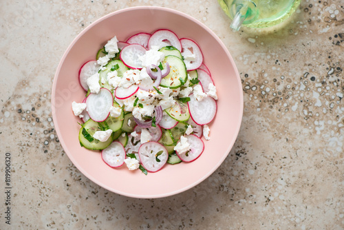 Roseate bowl with cucumber, radish and feta cheese salad, top view on a beige granite background, horizontal shot with space