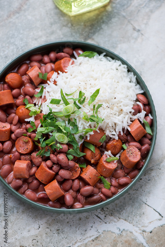 Plate of red beans with sausage and white rice on a light-grey granite background, vertical shot