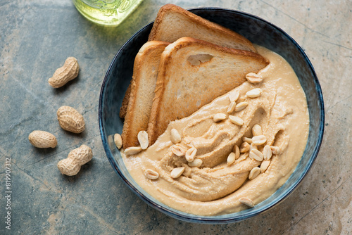 Bowl of peanut butter with toasted bread on a grey and beige granite background, horizontal shot, elevated view