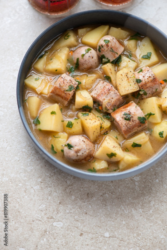 Plate of dublin coddle or irish sausage and potato stew, vertical shot on a beige stone background, high angle view