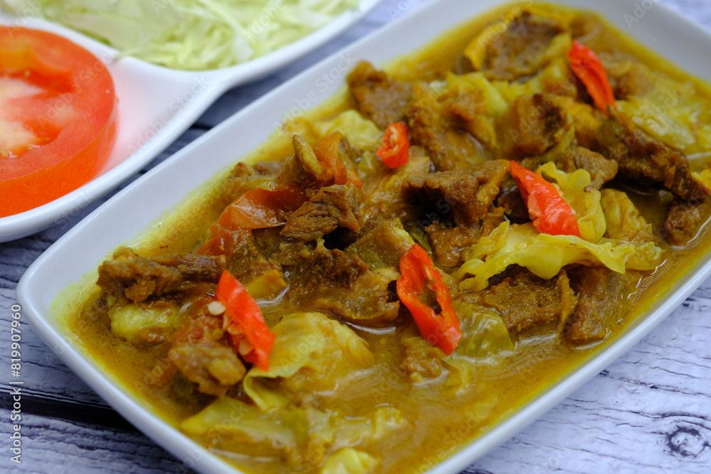 tongseng sapi is a traditional Indonesian dish made from beef, spices, coconut milk, cabbage, tomatoes, and chili. Tongseng on a wooden table with vegetables and tomatoes. Indonesian food. tongseng sapi is a traditional Indonesian dish made from beef, spices, coconut milk, cabbage, tomatoes, and chili. Tongseng on a wooden table with vegetables and tomatoes. Indonesian food.