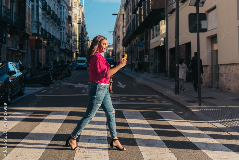 Trans woman walking in zebra pass and using cellphone at sunset. LGBT lifestyle.