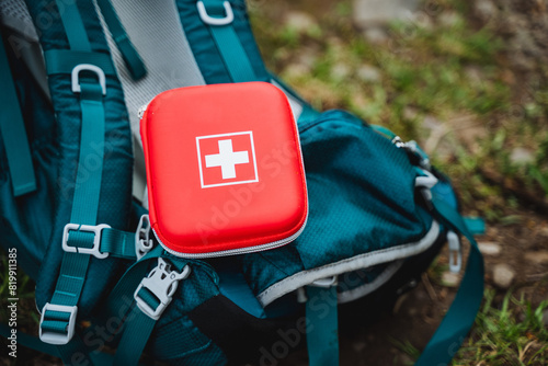 An electric blue first aid kit is placed on a blue backpack, surrounded by automotive exterior items like luggage, bumper, gas, and automotive tire