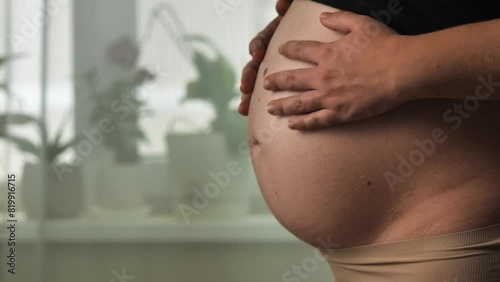 A close-up of beauty of a pregnant woman's belly. She is stroking it with her hands. The concept of joy and anticipation of motherhood. 32 weeks of pregnancy. warmth, love and miracle of new life