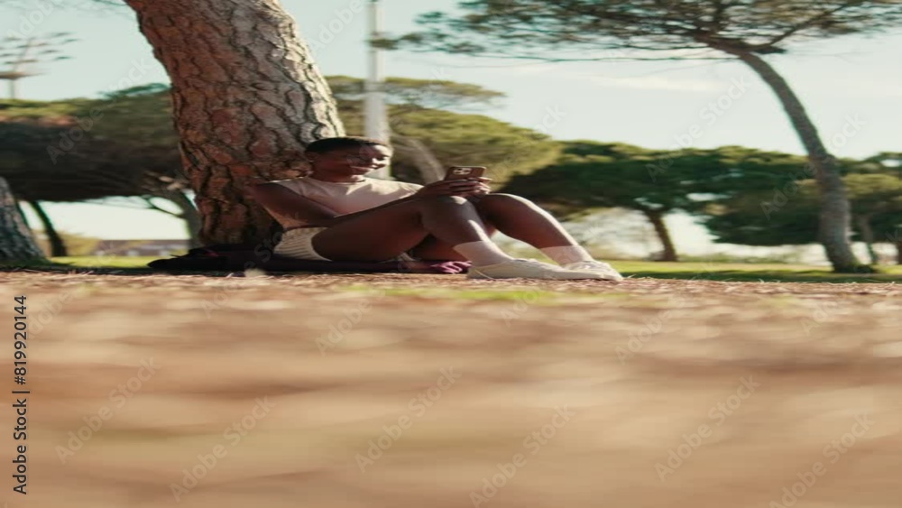 Vertical video of a girl sits in the park under a tree with a smartphone in her hands, ground focus Vertical video of a girl sits in the park under a tree with a smartphone in her hands, ground focus