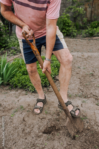 An adult man, a retired gardener, digs soil with a shovel in his hands in the spring in the garden outdoors. Agriculture concept.