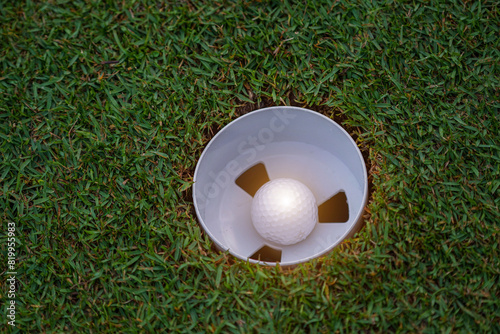 Top view of a golf ball on green course at hole. Golf ball and golf club on green in the evening golf course with sunshine