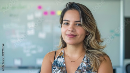 Smiling woman with long hair wearing a floral top standing in front of a whiteboard with notes and stickers.