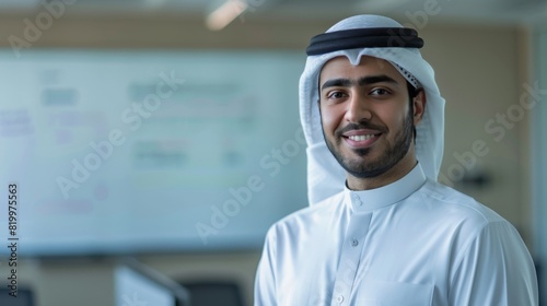 Smiling man in white agal and kandura standing in front of a whiteboard with writing. photo