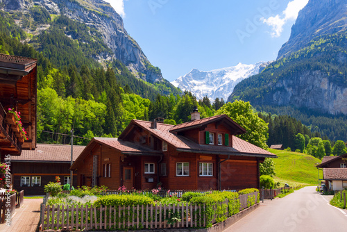 A cozy guest shalet in a traditional style against the background of snow-capped alpina peaks and bright green vegetation in the popular tourist area Grindelwald