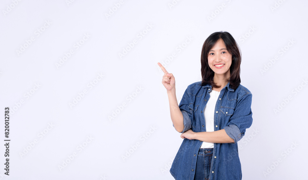 A young asian woman wearing denim jean while pointing finger to free copy space isolated on white studio background A young asian woman wearing denim jean while pointing finger to free copy space isolated on white studio background