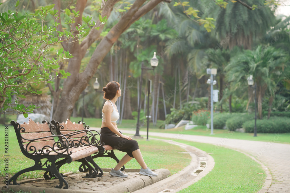Woman jogger refreshing and sitting over bench in a park after running Woman jogger refreshing and sitting over bench in a park after running