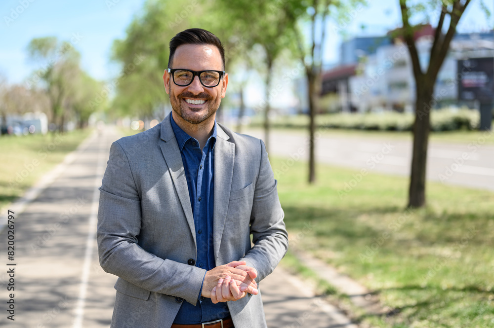 Portrait of contented young businessman with hands clasped smiling and standing on city street Portrait of contented young businessman with hands clasped smiling and standing on city street