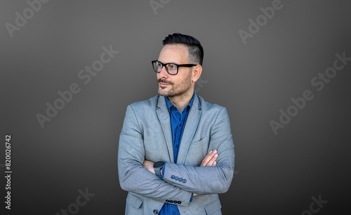 Confident young businessman with arms crossed looking away and thinking ideas on gray background
