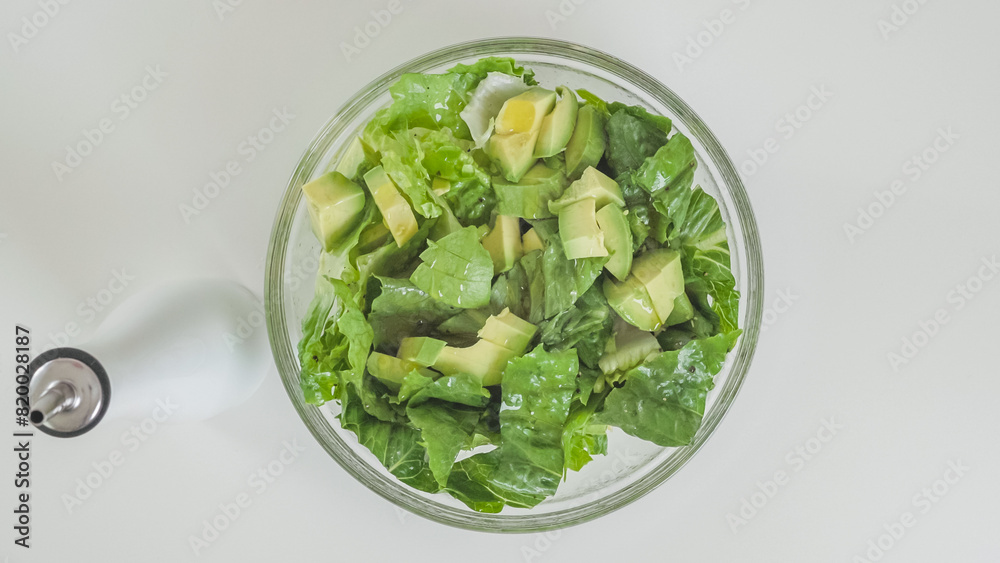 Romaine lettuce, celery, and avocado salad in a glass bowl on white kitchen table, view from above Romaine lettuce, celery, and avocado salad in a glass bowl on white kitchen table, view from above