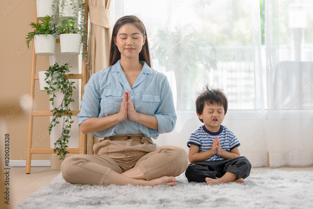 Heartwarming of mother and her young child yoga meditating together at home. Sit cross-legged on a soft rug, hands in prayer position, eyes closed, embodying tranquility and shared mindfulness