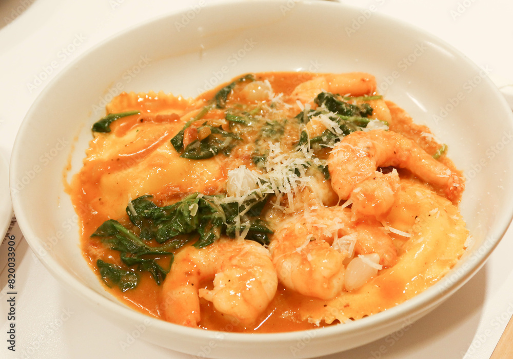 close up of shrimp prawns seafood sauce ravioli with spinach on a white plate. cheese are spread on the top. close up of shrimp prawns seafood sauce ravioli with spinach on a white plate. cheese are spread on the top.