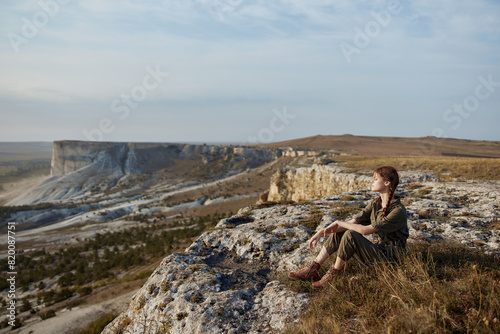Woman sitting on cliff edge admiring breathtaking valley and majestic mountains in travel destination scene of serenity and beauty © SHOTPRIME STUDIO