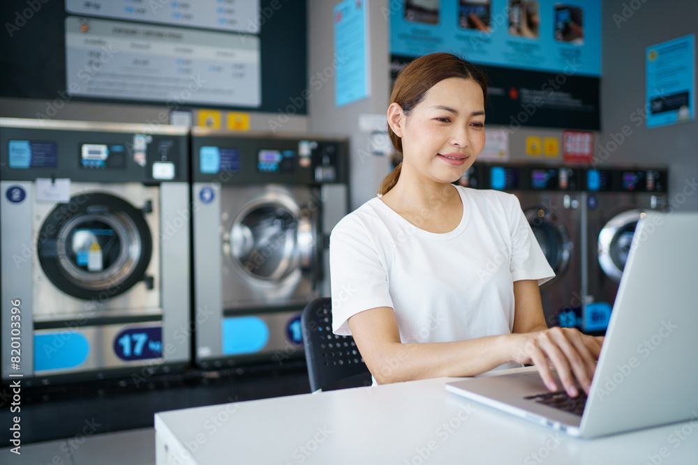 Woman working on laptop computer while waiting her clothes washed. Woman working on laptop computer while waiting her clothes washed.