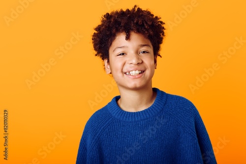 Bright and cheerful a joyful young african american boy in a blue sweater against a vibrant orange backdrop